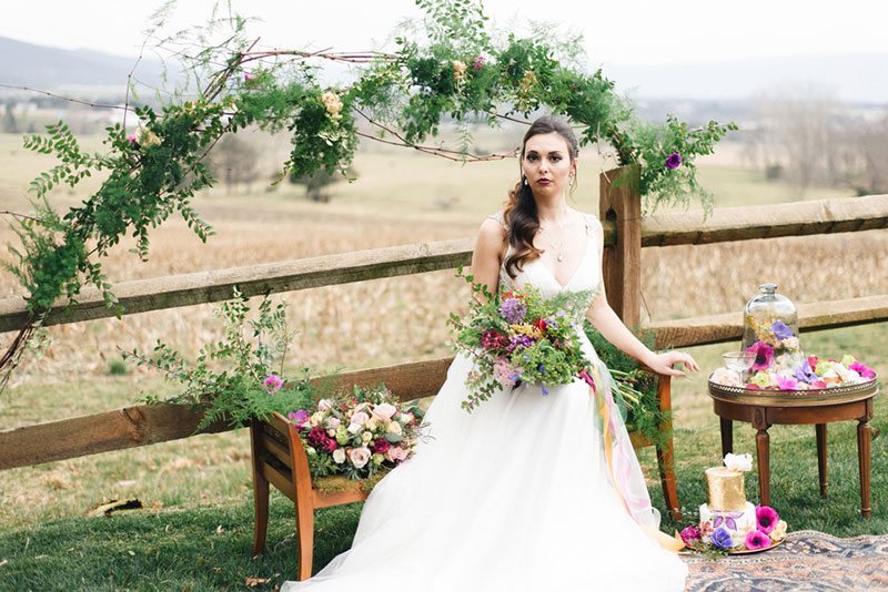 Outdoor_wedding_with_pops_of_color-bride_holding_flowers_on_bench