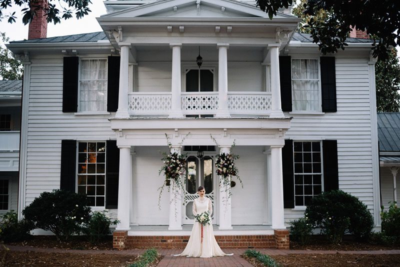 Vintage_Winter_Bridal-bride_holding_flowers_in_front_of_house