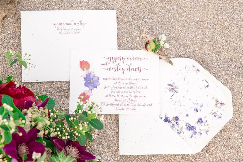 Chic_Coastal_Wedding-invitations_on_sand_with_flowers
