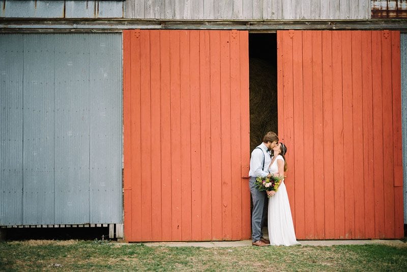 Modern Boho Bride And Groom Kissing In Front Of Red Door