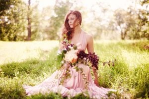 Pink Wedding Bride Sitting In Field With Flowers