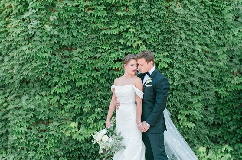 Chic And Modern Bride And Groom In Front Of Bushes