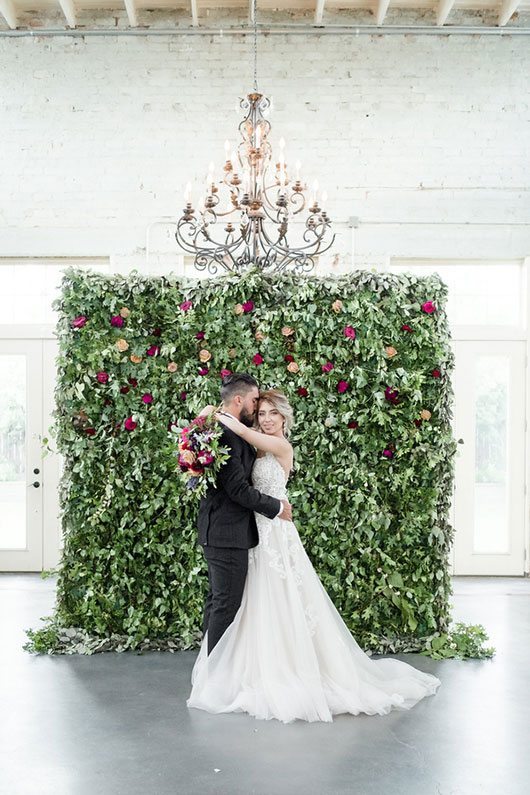 Vintage Copper Bride And Groom Hugging In Front Of Flower Wall