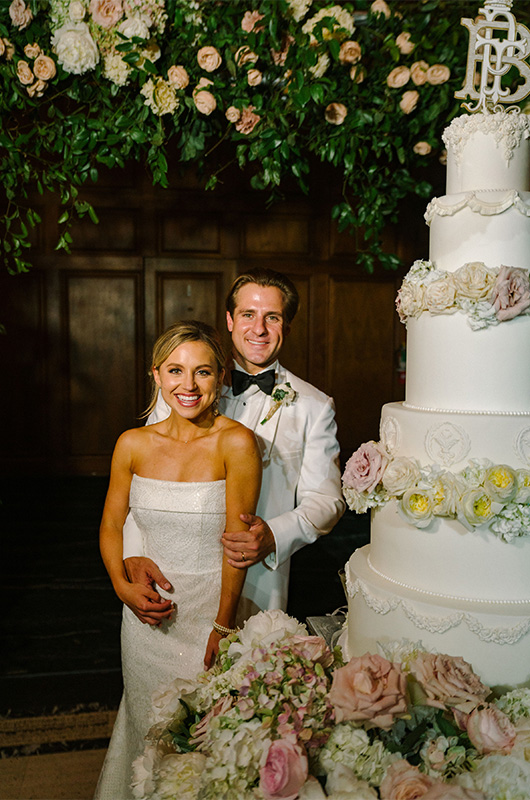 Peyton LoCicero and James Trist Marry in an Extravagant New Orleans Wedding couple pose in front of cake copy